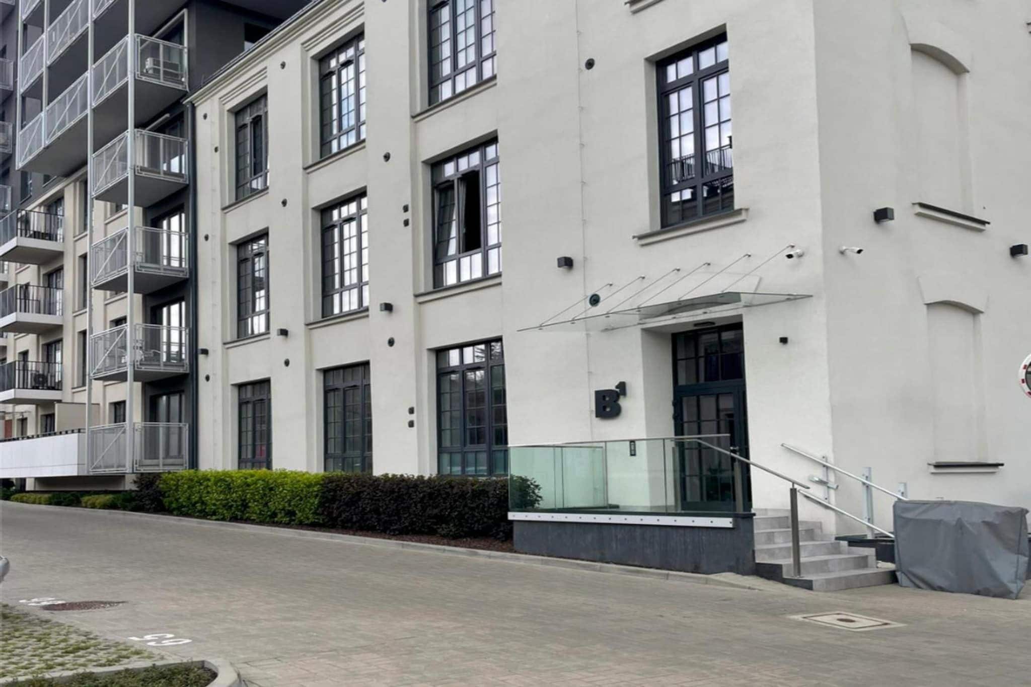 Un immeuble résidentiel moderne à plusieurs étages, doté de balcons, de grandes fenêtres et d’une entrée abritée.