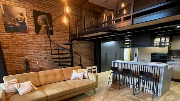 Ein modernes Wohnzimmer mit einer Couch, einem Essbereich mit Barhocker und einer Küche im Hintergrund.