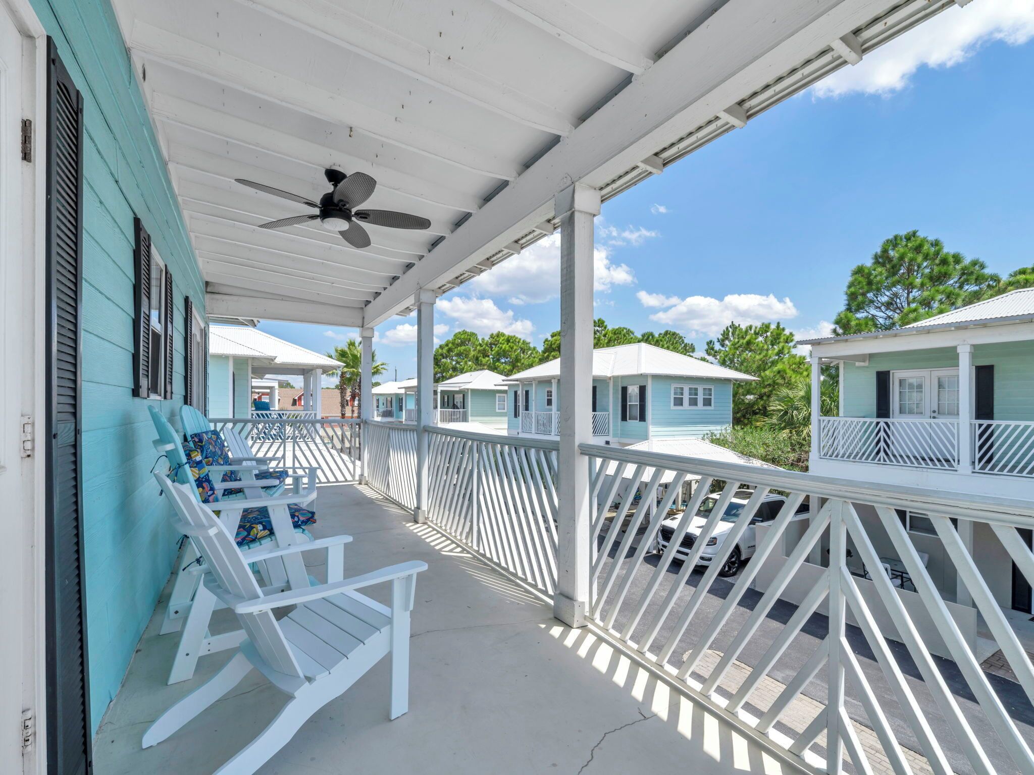 A covered porch with white railings and a ceiling fan, featuring two white rocking chairs and a table.
