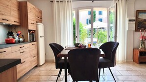 A kitchen with wooden cabinets, a dining table with chairs, and a view through a glass door to an outdoor area.