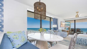 Una habitación con una mesa redonda, sofá azul con estampado y vista al océano.