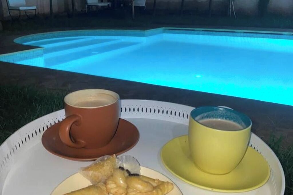 A tray with a cup of coffee and a cup of tea, and a plate with pastries, placed near a pool.