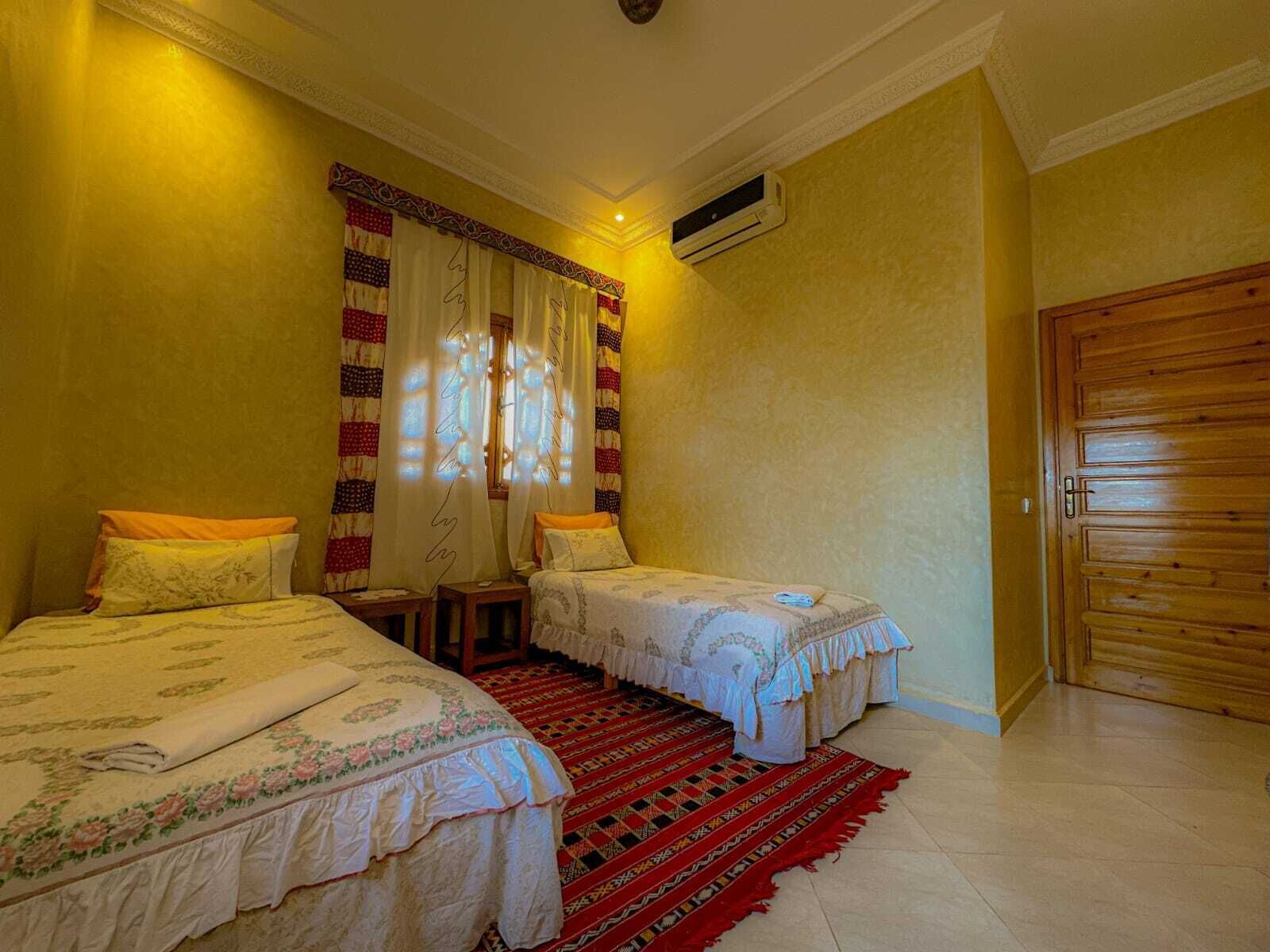 A bedroom with two beds, a red patterned rug, and a wooden door.