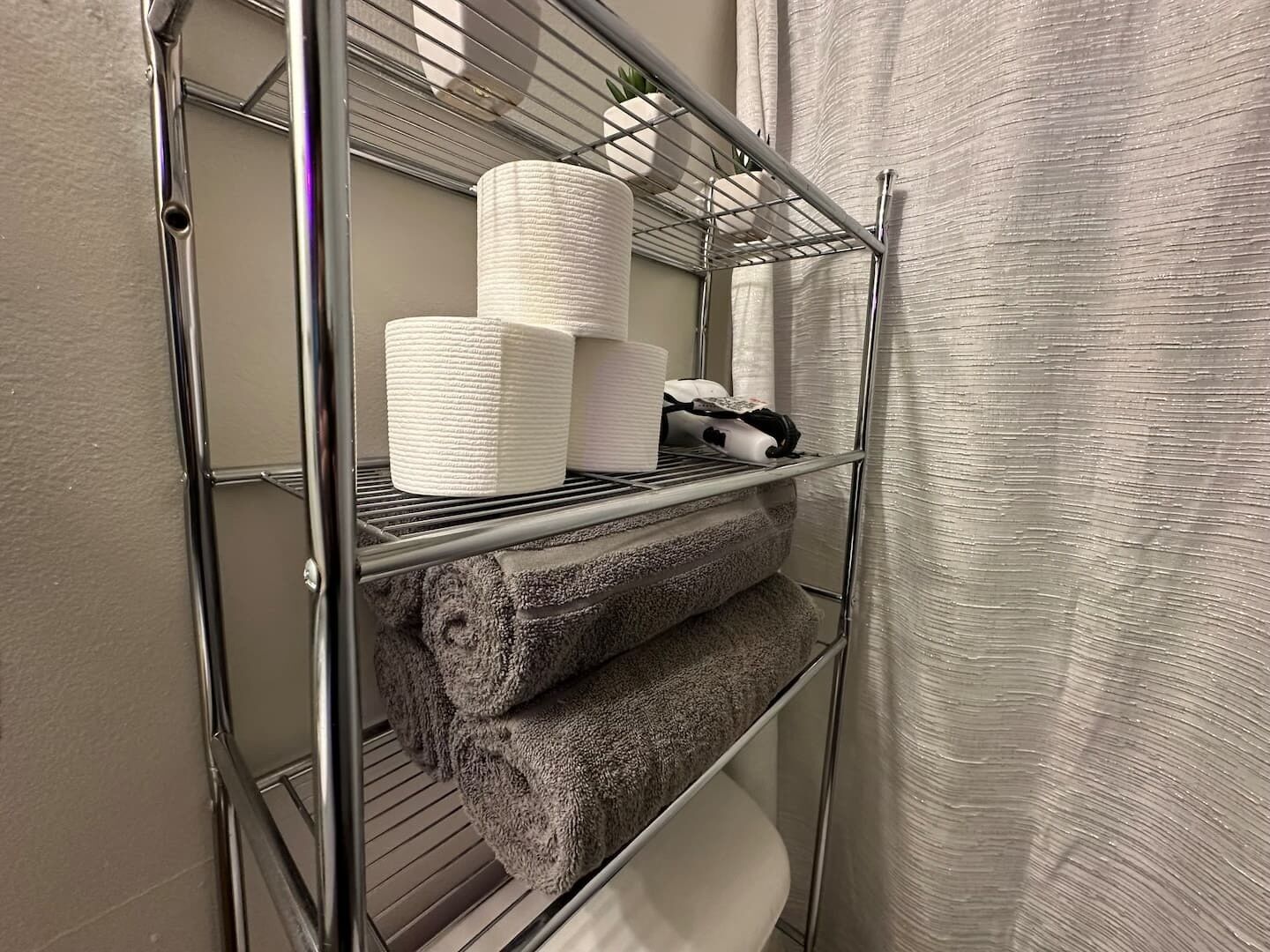 A metal shelf unit with towels and toilet paper.