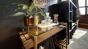Een moderne woonkamer met een salontafel met glazen blad, een potplant, decoratief glaswerk en een lijstwerk aan de muur.