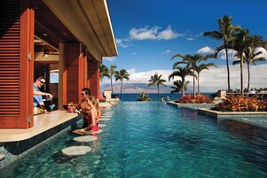 Piscina de resort con agua cristalina, palmeras y vista al océano.