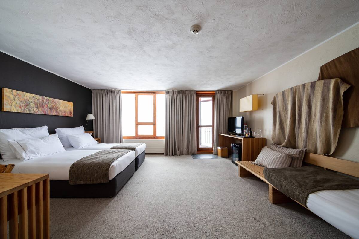A hotel room with two beds, a desk, a TV, and a large window.