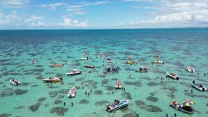 Una spiaggia tropicale con numerose imbarcazioni e persone che si godono le acque cristalline.