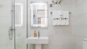 A modern bathroom with a glass shower enclosure, a white sink with a soap dispenser, and two towels hanging on a rack.