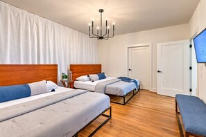 A hotel room with two beds, a wooden headboard, a bedside table with a lamp, and a television on the wall. - Premium Home Rooftop Pool Table 13 Beds (Nashville)