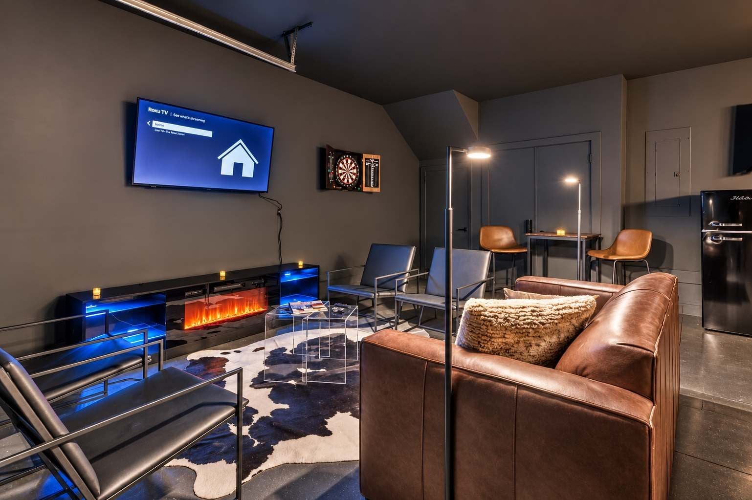 Uma sala de estar moderna com televisão de tela plana, lareira, assentos de couro e área de cozinha.
