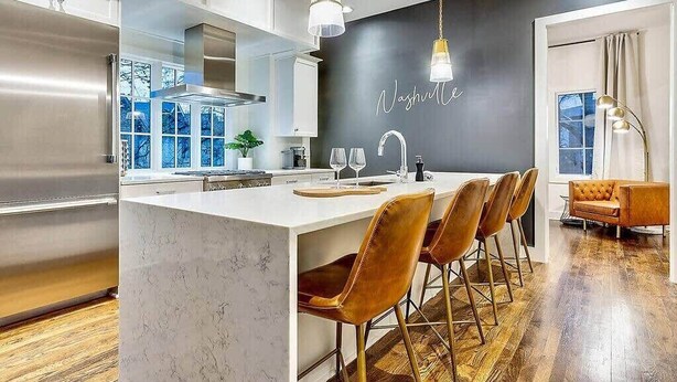 Une cuisine moderne dotée d’un îlot en marbre, d’appareils électroménagers en acier inoxydable et d’un mur d’accent noir sur lequel est inscrit le mot « Nashville ».