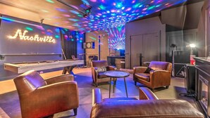 Un espace salon confortable avec des fauteuils en cuir, une table de billard et un panneau lumineux au néon sur lequel on peut lire « Nashville ».