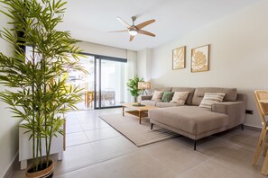 Una sala moderna con un sofá beige, una mesa de centro, una lámpara de pie y una planta grande en maceta.