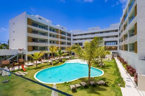Un hotel moderno con piscina, mobiliario exterior y un jardín bien cuidado.