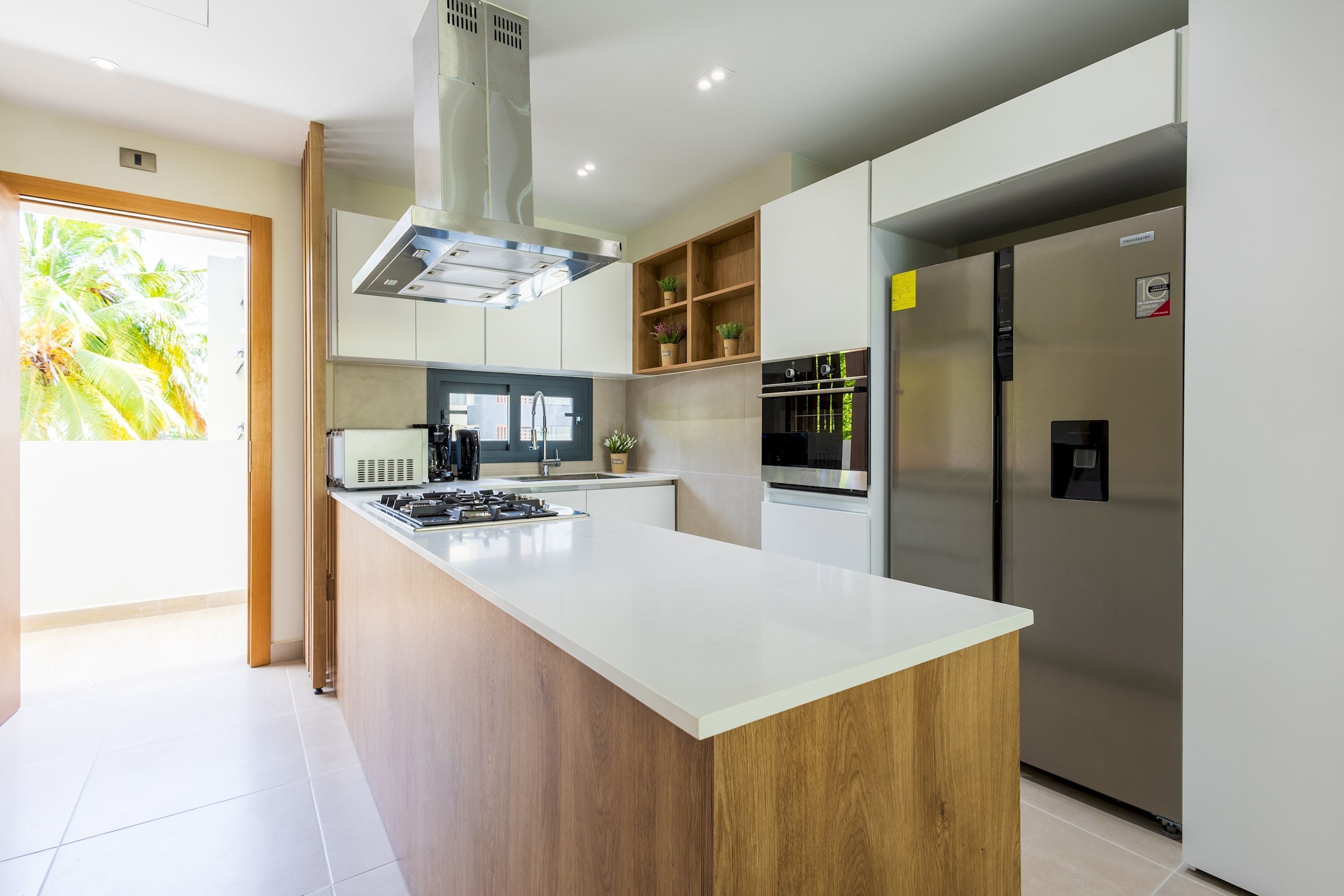 Een moderne keuken met een centraal eiland, roestvrijstalen apparatuur en uitzicht op groen.