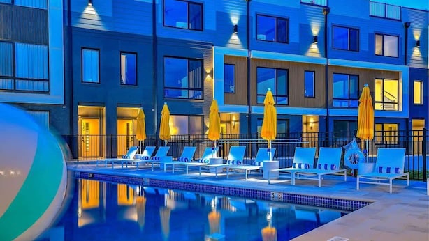 Ein modernes Hotel mit Poolbereich, mehreren Liegestühlen und gelben Sonnenschirmen.