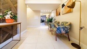 A hallway with a modern design, featuring a patterned wall, a potted plant, a table, and a row of chairs. - Apt 4min From sea in BC Close to Everything Rta042 (Balneário Camboriú)