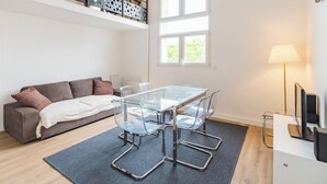A modern living room with a glass-top dining table, clear chairs, a grey sofa, a wooden floor, and a window with natural light. - Le Duplex du Port: Parking, Paimpol Center (Paimpol)