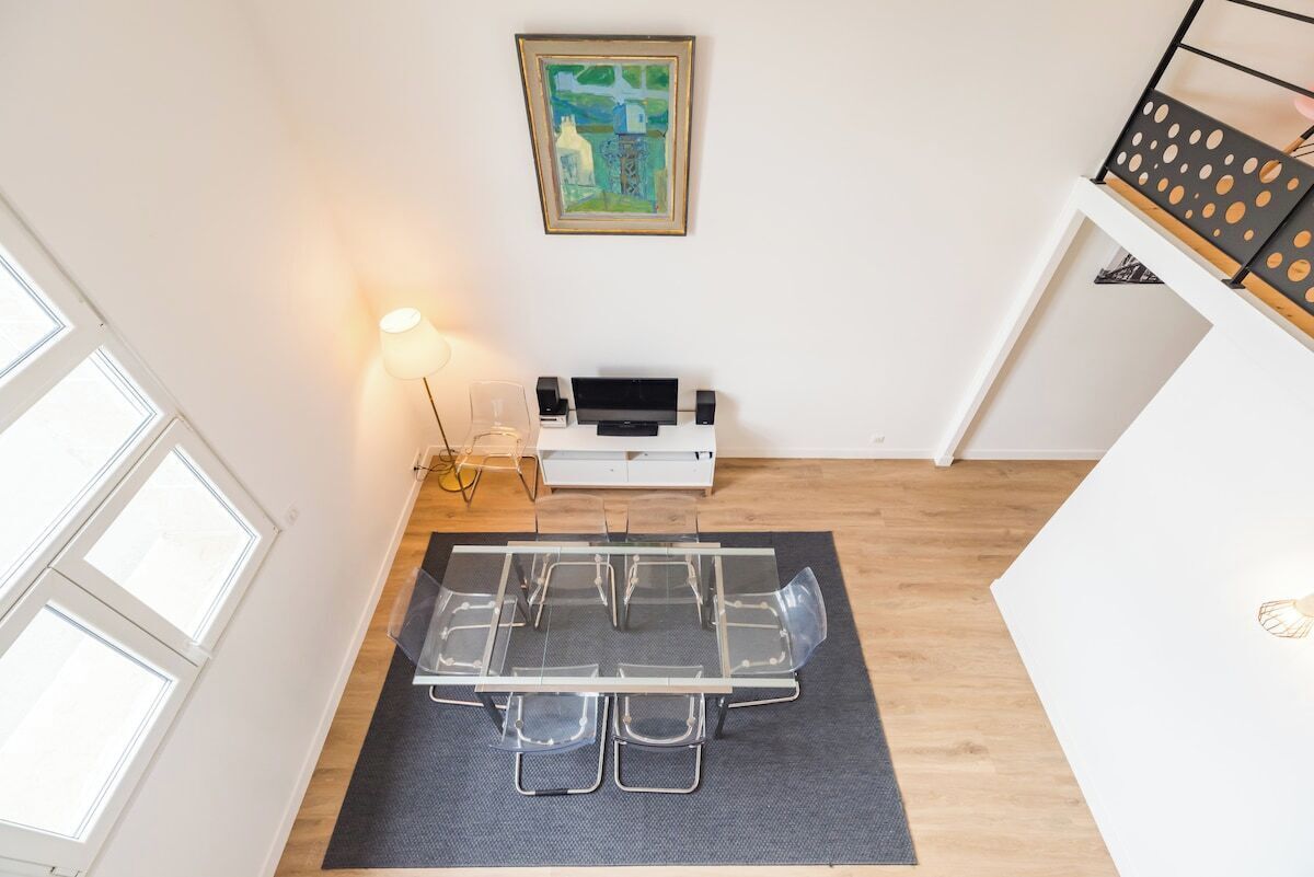 Een eetgedeelte met een glazen tafel en stoelen, een lamp, een lijst met een schilderij en een wit kastje.