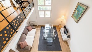A modern living room with a glass-top dining table, a sofa with cushions, a black floor mat, a standing lamp, and a framed artwork on the wall. - Le Duplex du Port: Parking, Paimpol Center (Paimpol)