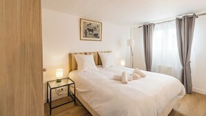 A neatly made bed with white linens, a bedside table with a lamp, and a framed picture on the wall. - Le Duplex du Port: Parking, Paimpol Center (Paimpol)