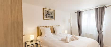 A neatly made bed with white linens, a bedside table with a lamp, and a framed picture on the wall.