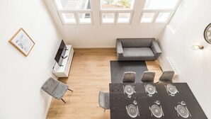 A modern living room with a gray sofa, a dining table set for four, and a TV on a white stand.