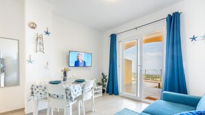 Una sala de estar moderna con comedor, televisor y balcón con cortinas azules.