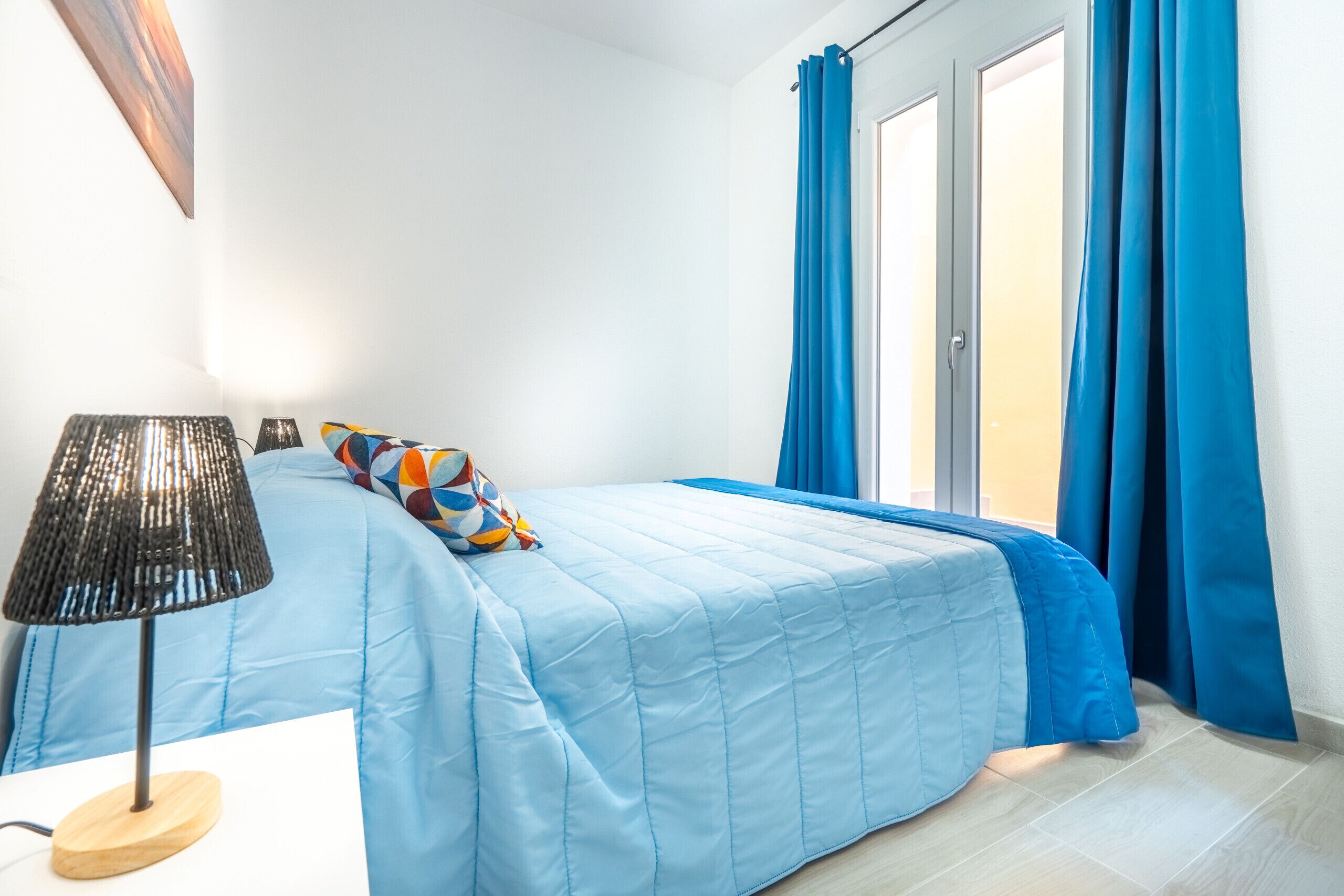 Un dormitorio con cama, lámpara y cortinas.