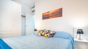 Un dormitorio con cama, almohadas, mesita de noche, lámpara, cuadro y armario.