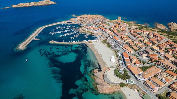 Vista aérea de un pueblo costero con un puerto deportivo, edificios y una iglesia destacada.