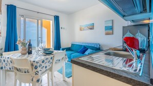 Una cocina compacta con un lavamanos, un hervidor rojo y un comedor con una mesa lista para dos.