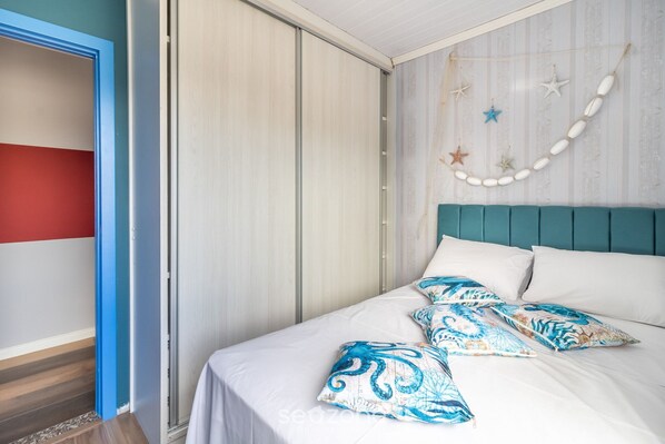 A bedroom with a bed, white bedding, teal headboard, and decorative starfish on the wall.