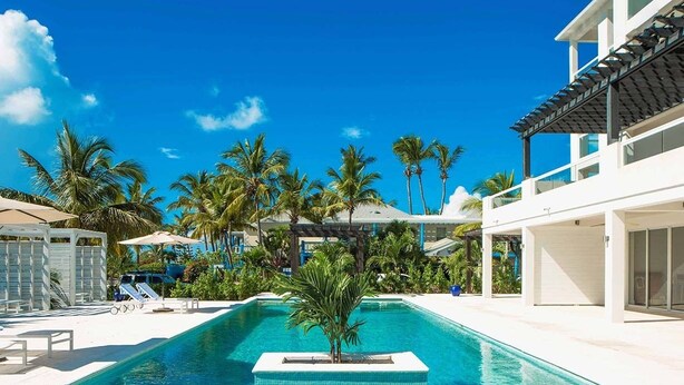 A swimming pool with clear blue water, surrounded by palm trees and a white building with a modern design. - The Tides Grace Bay (Providenciales)