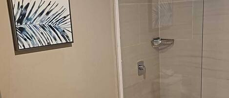 A bathroom with a toilet, a glass shower enclosure, and a framed picture on the wall.
