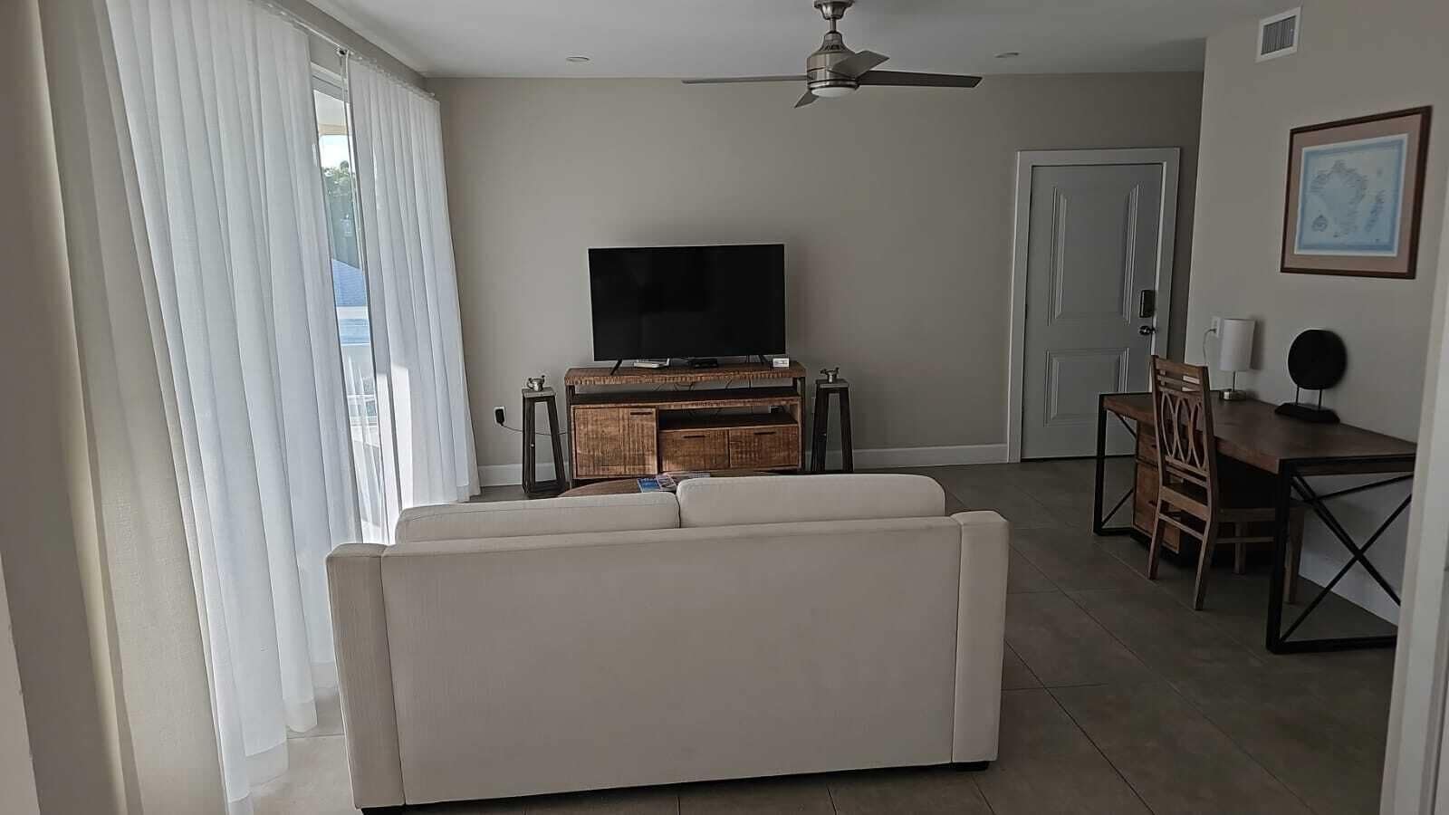 A living room with a sofa, a TV, a dining table with chairs, and a ceiling fan.
