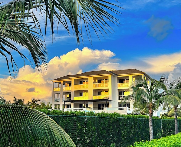 A multi-story hotel with balconies, surrounded by greenery and palm trees.