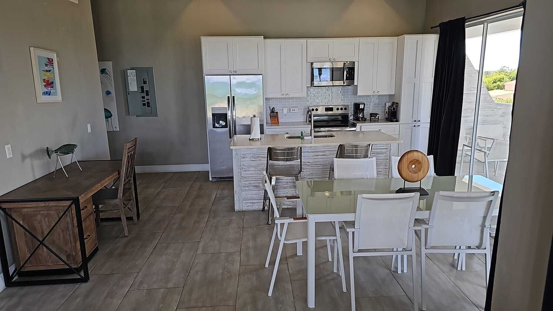 A modern kitchen with white cabinets, a central island with seating, and a dining area with a wooden table and chairs.