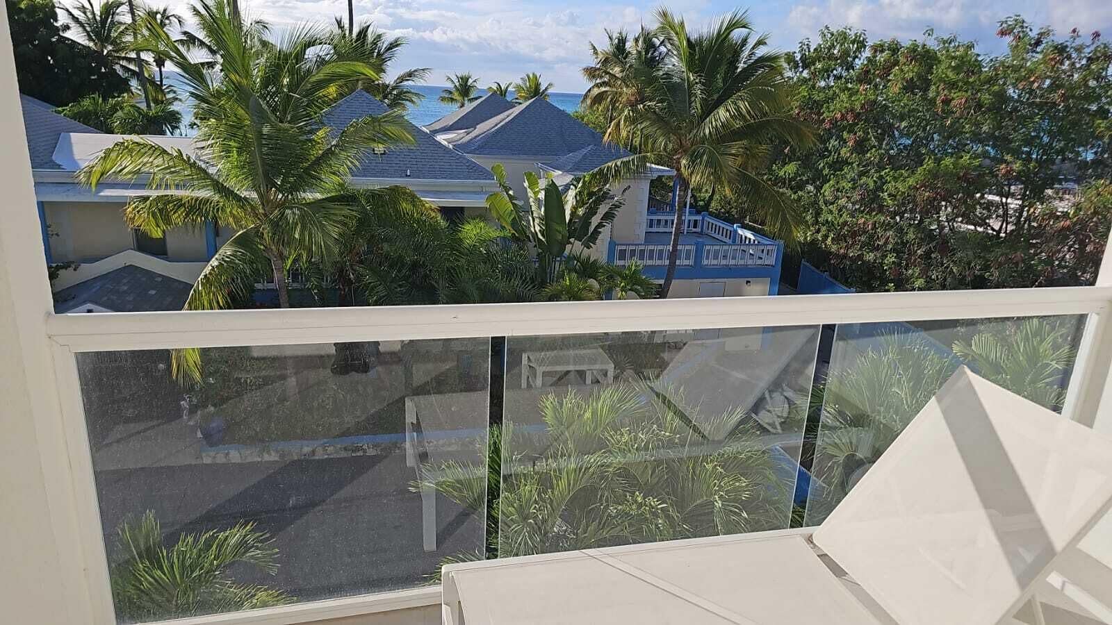 Un balcon offrant une vue sur une zone touristique, avec des palmiers et des bâtiments aux toits bleus.