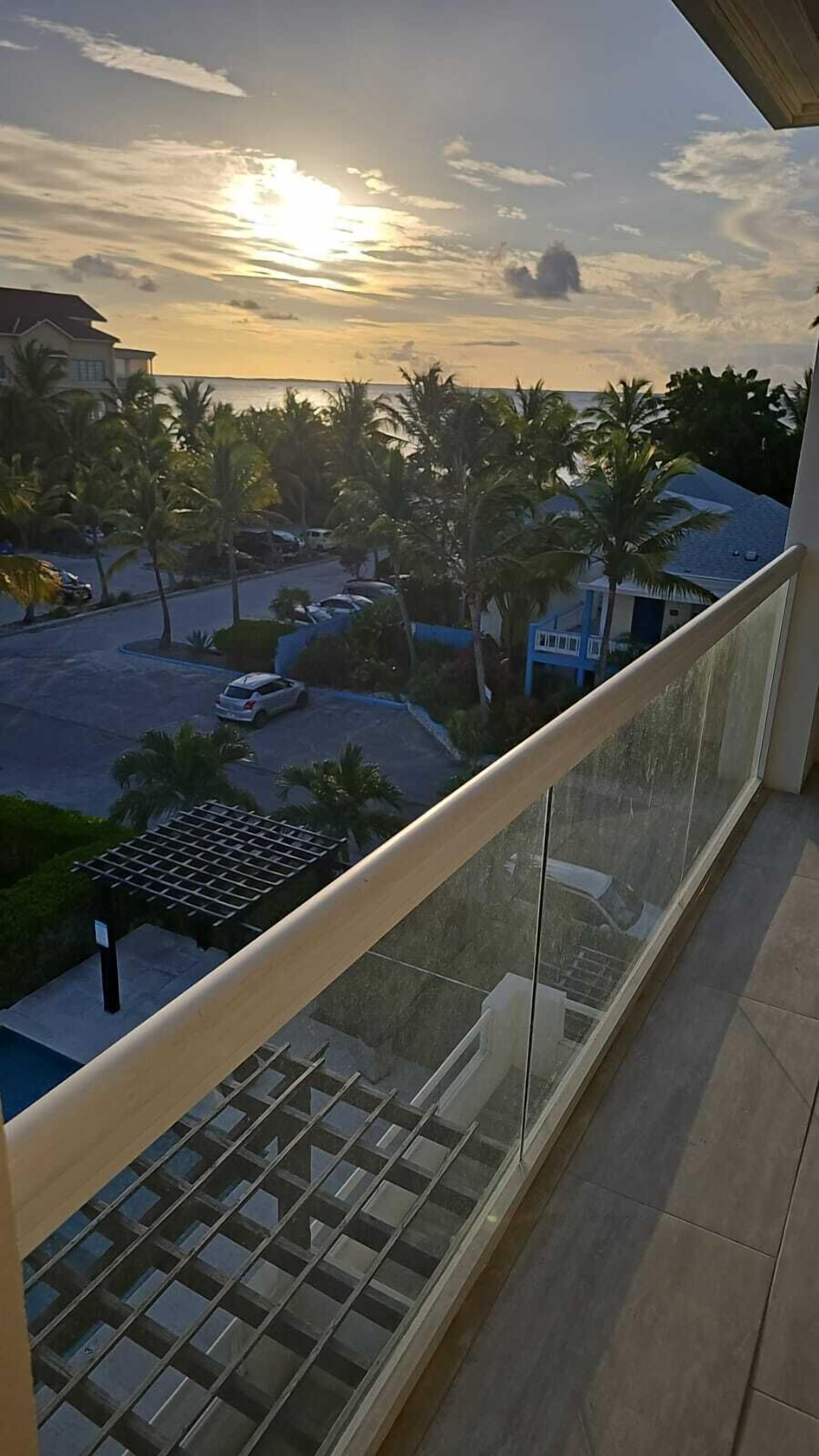 Un balcón con vistas a un estacionamiento, palmeras y un edificio con techo azul.