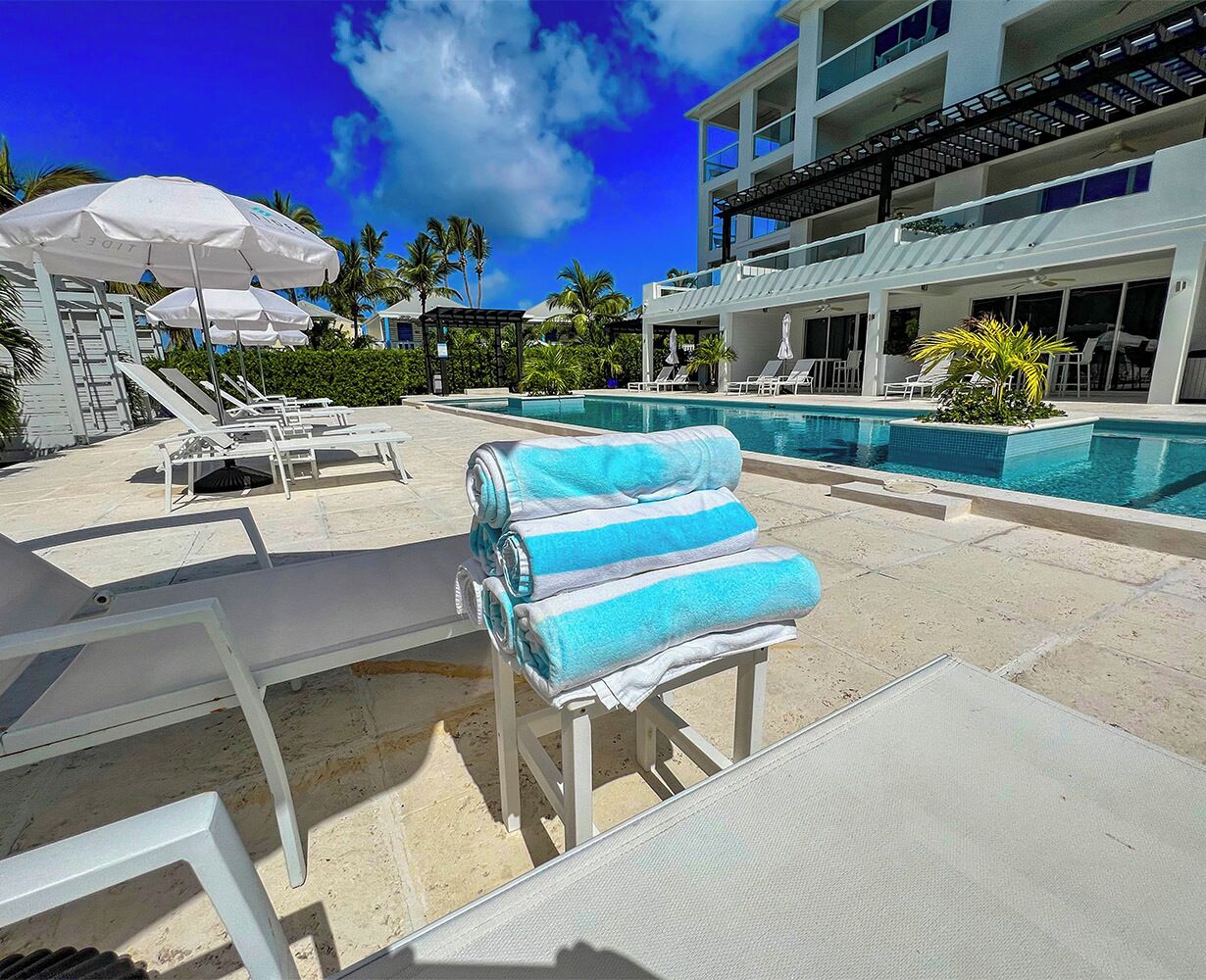 A poolside area with lounge chairs, umbrellas, and a building with balconies.
