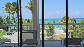 A balcony with two chairs and a table, overlooking a beach with palm trees and a clear blue sky. - The Tides Grace Bay (Providenciales)