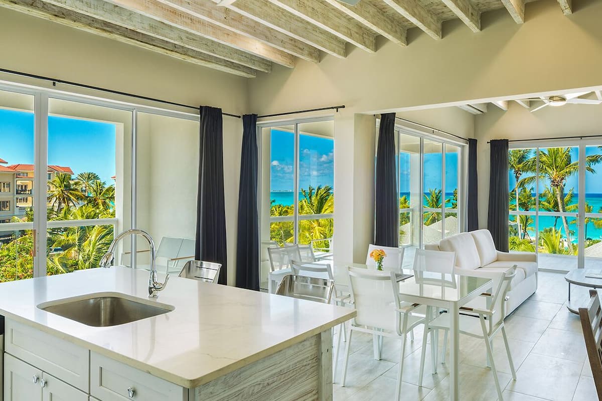 A modern kitchen with a large island, white furniture, and large windows offering ocean views.