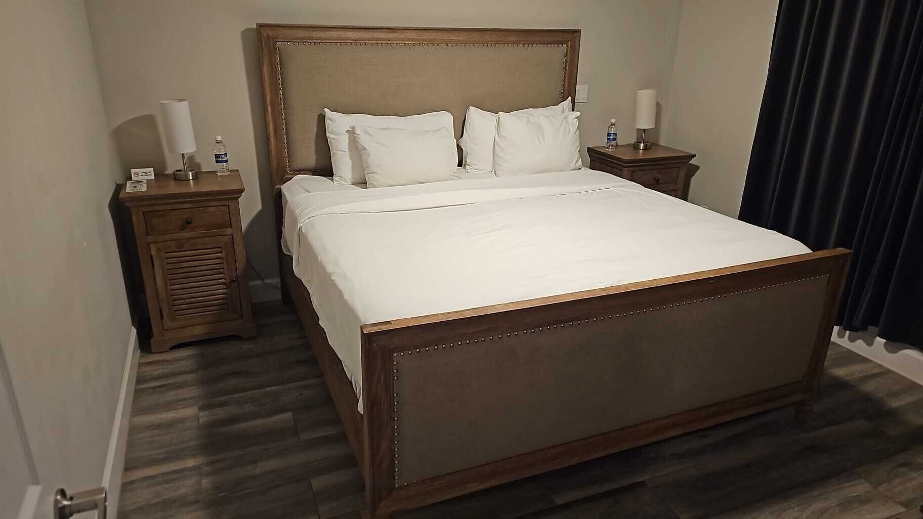 A hotel room with a large bed, two bedside tables, a nightstand, and a wooden floor.