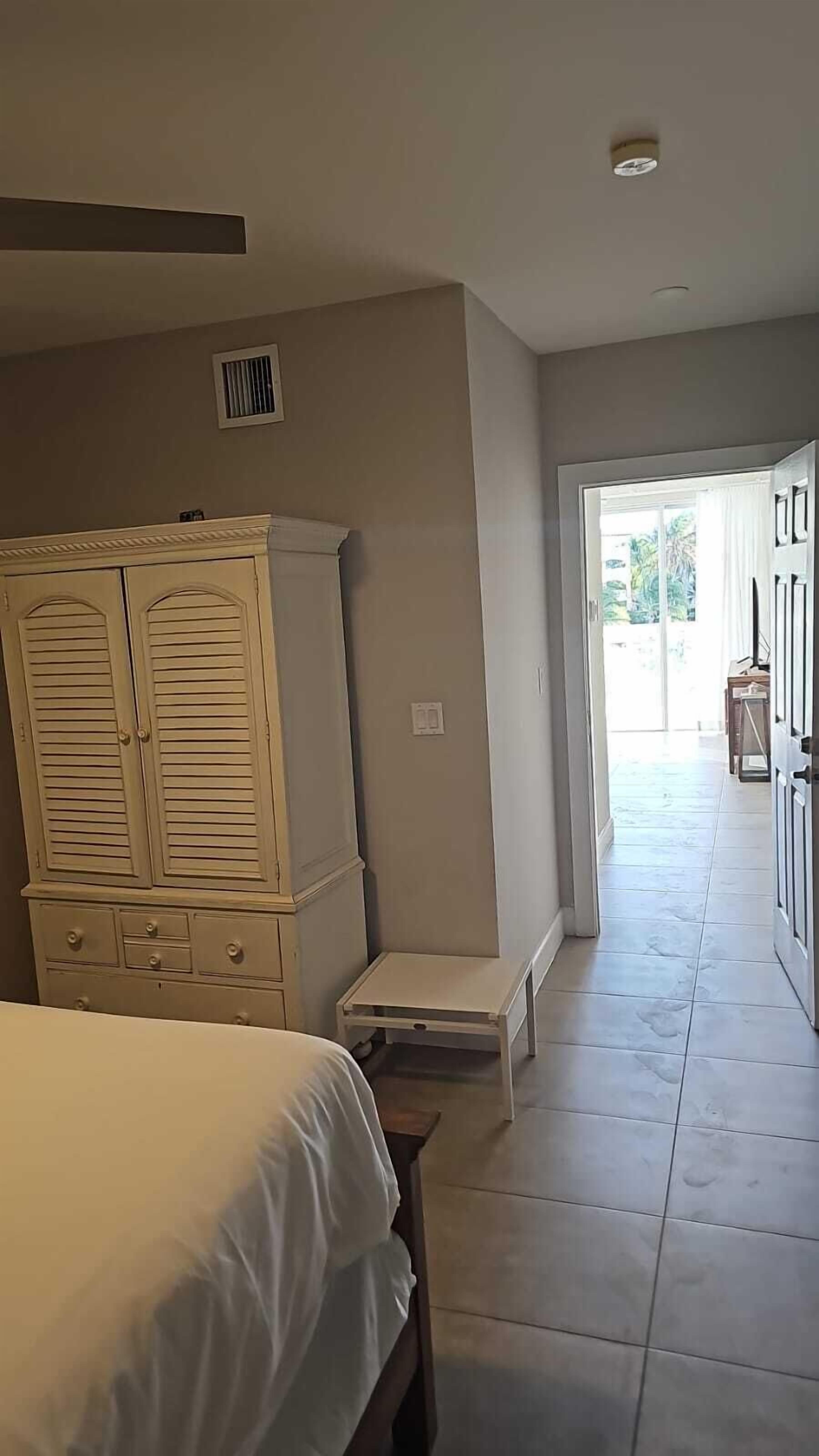 A bedroom with a bed, a dresser, and a small table. There is a door leading to a balcony.