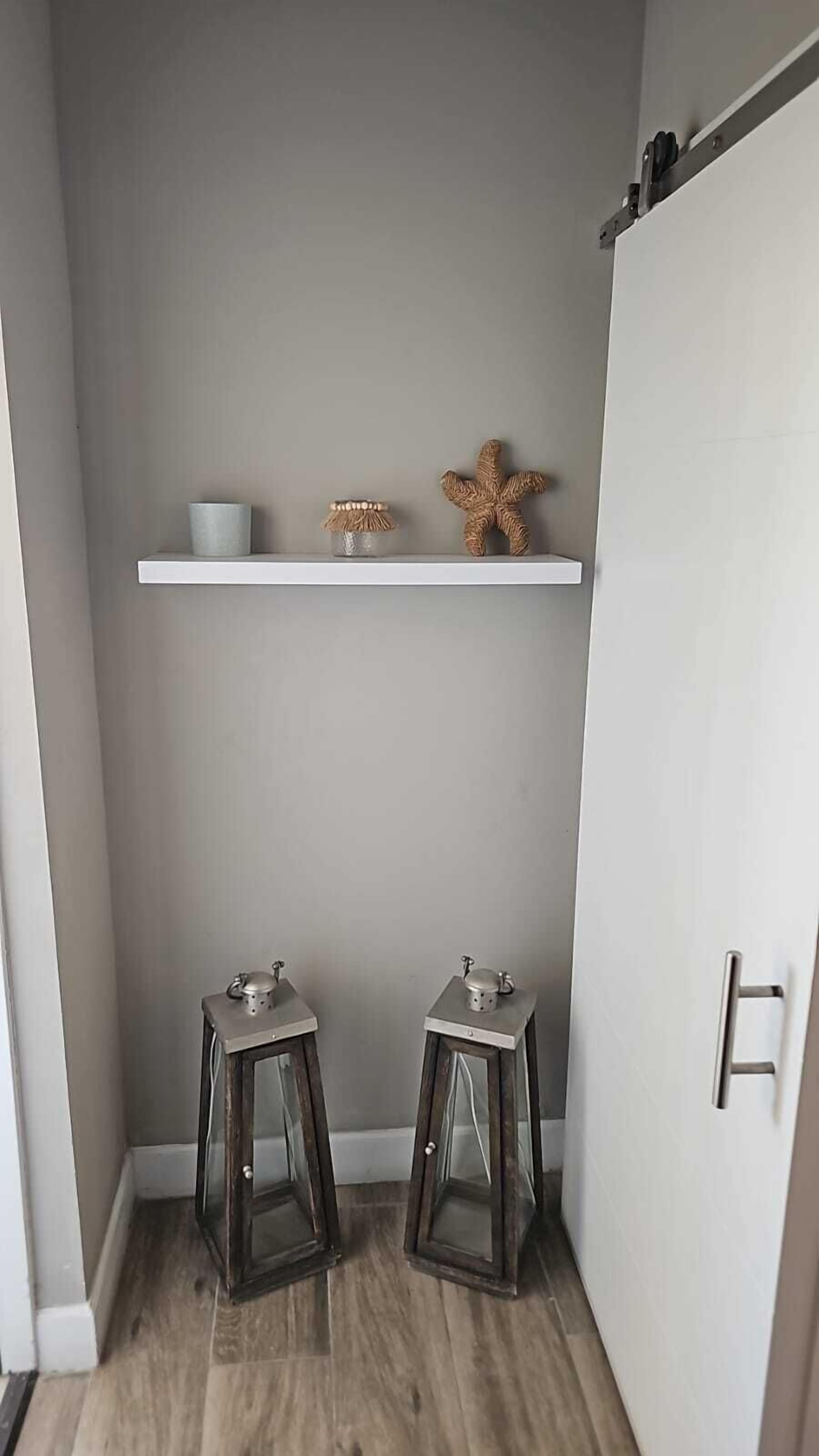 Un bagno piccolo con un mobile lavabo bianco, due sgabelli, uno scaffale con oggetti decorativi e un armadietto.