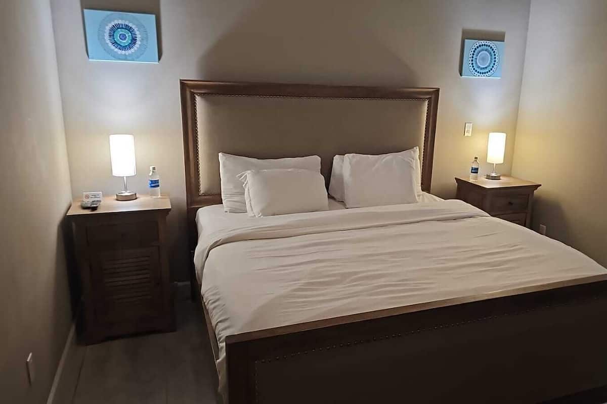 A neatly made bed with a wooden headboard and two bedside tables, each with a lamp and a bottle of water.