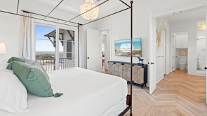 Quarto com cama de dossel, lustre, televisão e vista para a praia.