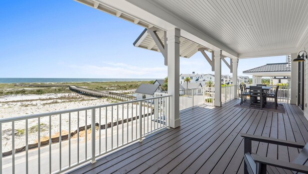Um deck de madeira com guarda-corpo, de frente para uma praia e o oceano.